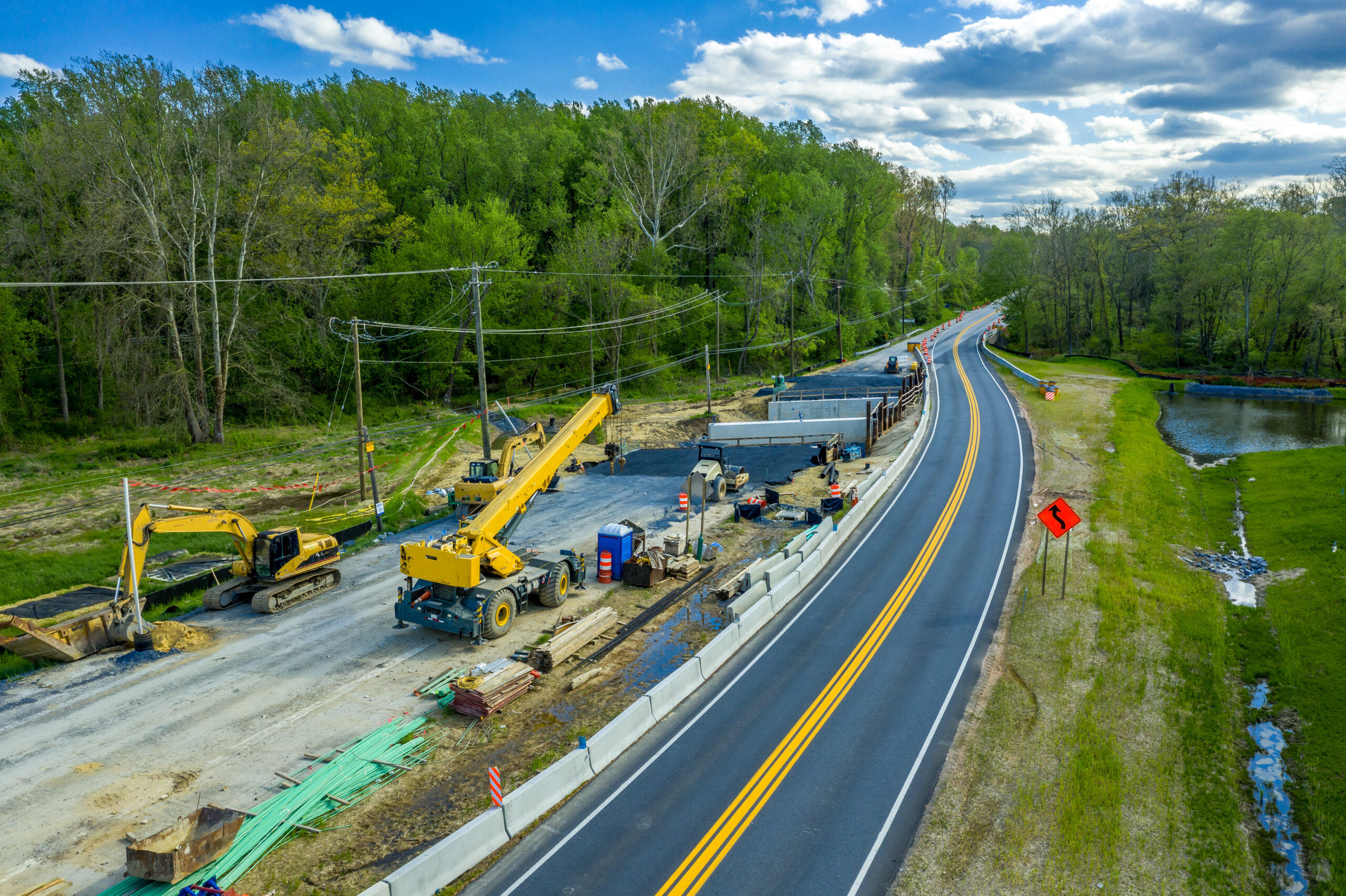 Aerial view of expanding a two lane road to a four lane highway with heavy construction equipment such as cranes parked for the weekend before a small bridge is completed